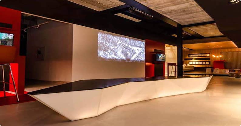 Móveis planejados em espaço corporativo moderno com balcão de design geométrico iluminado, projetor em parede e decoração contemporânea