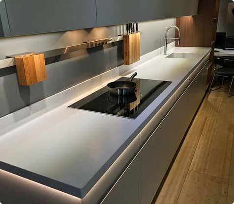 Móveis planejados em cozinha moderna com bancada branca, placa de indução preta, torneira metálica e armários cinzentos minimalistas